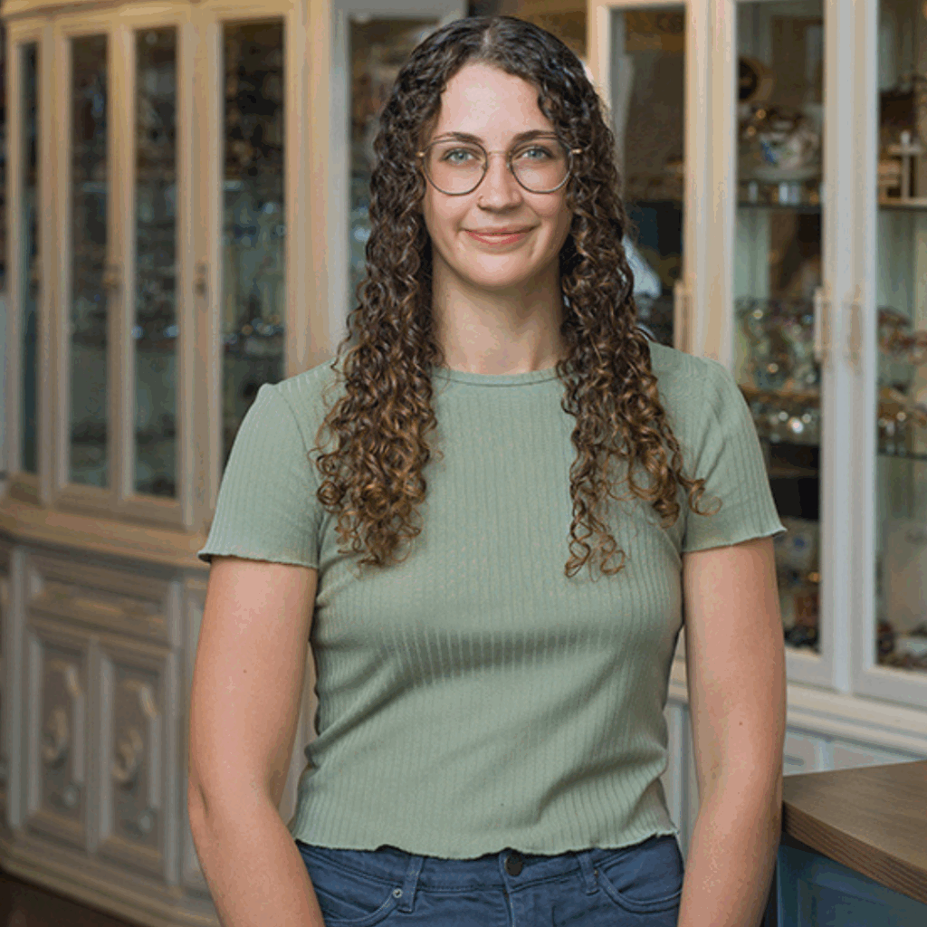 Headshot of Inspired Eyes Kelowna optical team member wearing round eyeglasses in front of display cabinets