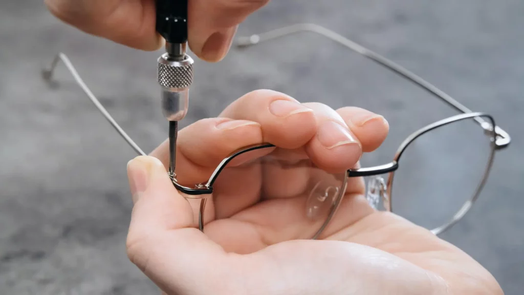 Close-up of hands repairing metal eyeglass frames with a screwdriver